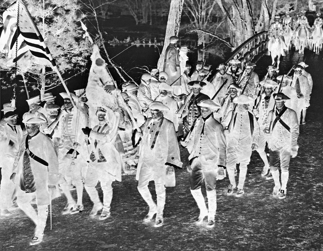 “Militiamen” march across Concord Bridge in 1925. Note “Indians” in canoes in left background. (Joseph Bilby Collection)